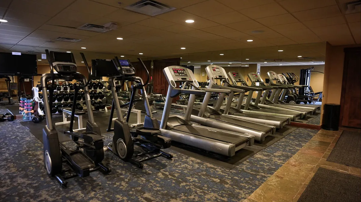 An energetic, modern fitness center interior featuring rows of elliptical machines, treadmills, and a dumbbell rack. The space is bright and inviting, ready for guests to maintain their fitness routines while traveling.