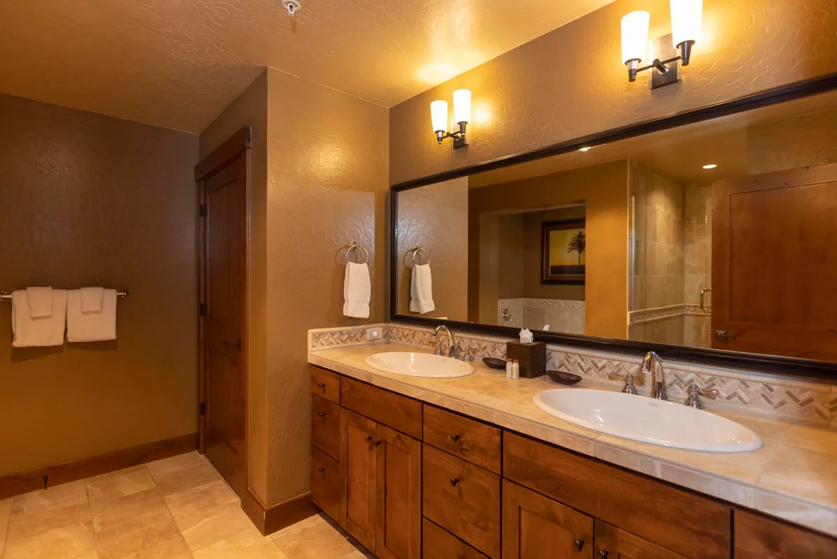 A modern bathroom with double vanity sinks, a large mirror, wooden cabinetry, and neatly arranged towels—creating a serene, spa-like atmosphere.