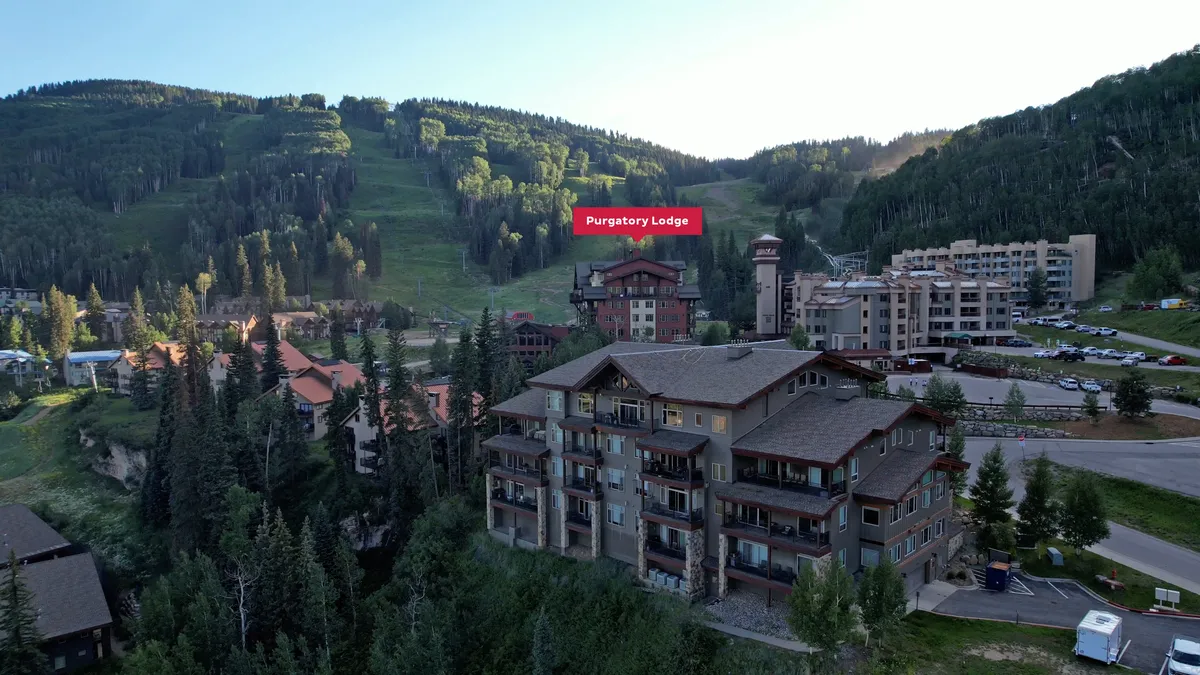 This exterior image showcases Purgatory Lodge surrounded by lush summer greenery and the breathtaking backdrop of the San Juan Mountains. Several nearby buildings hint at the vibrant Purgatory Village, while the open landscape suggests immediate access to hiking and biking trails.