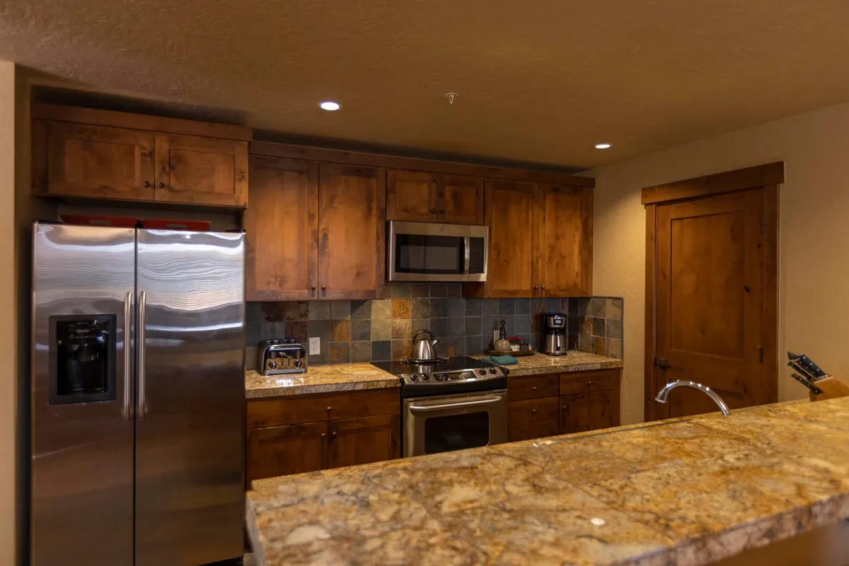 A cozy and functional kitchen scene, highlighting a long granite countertop, stainless steel appliances, rich wooden cabinetry, and a decorative tile backsplash. Sunlight filters in, suggesting a morning coffee or family breakfast atmosphere.